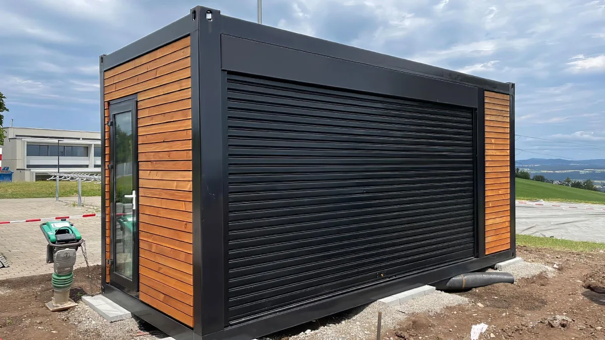 Ein braun-schwarzer Container steht auf einer Baustelle.